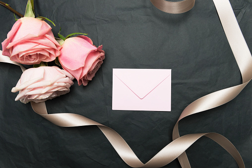 Pink envelope, pink roses and golden ribbon on black table.