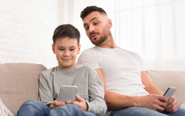 istock Curious dad peeking at his son smartphone at home 1217564371