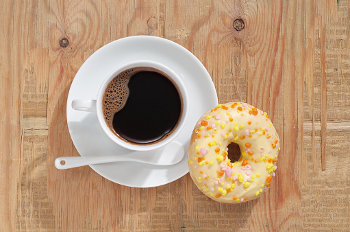 Cup of coffee with yellow donut on old wooden background, top view