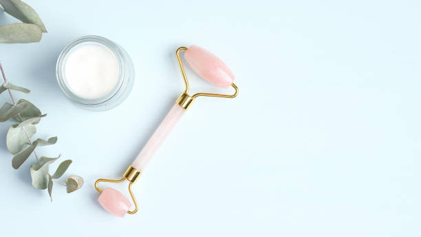 istock Rose quartz facial massage roller with moisturizer cream and eucalyptus leaf on blue background. Face massager with jade stone, anti-aging, anti-wrinkle beauty skincare tool 1217564396