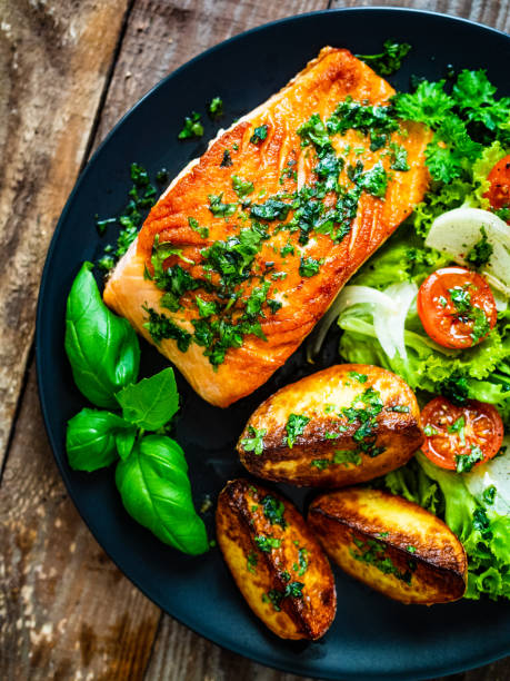 Fried salmon, fried potatoes and vegetables on wooden background