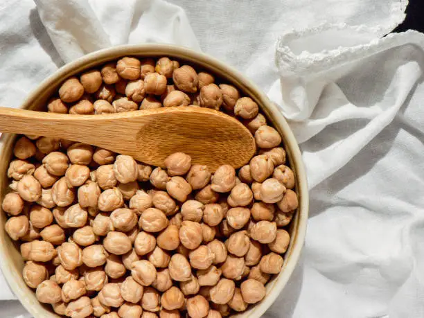 Dried uncooked chickpeas in a brown clay bowl wooden spoon on white tablecloth