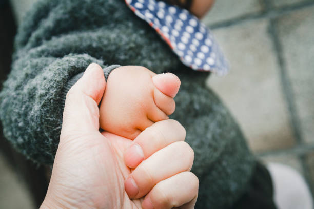 Description: Macro image of an infant's hand grasping the parent's thump. White Background.
