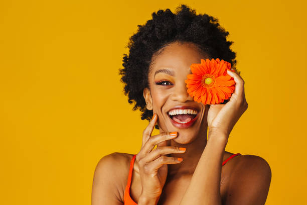 porträt einer glücklichen aufgeregten jungen frau mit orange gerbera gänseblümchen bedeckt ihr auge - dramatic make up stock-fotos und bilder