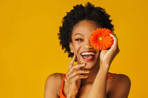 Photo of Portrait of a happy excited young woman holding orange gerbera daisy covering her eye