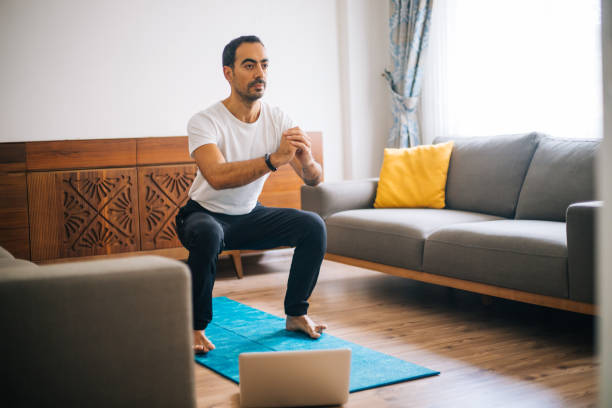 muscular athletic fit mann in t-shirt und shorts macht squat übungen zu hause - agrobacter stock-fotos und bilder