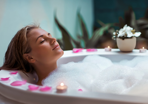 Portrait of a beautiful young woman taking bath with foam by candlelight, enjoying dayspa in luxury spa hotel