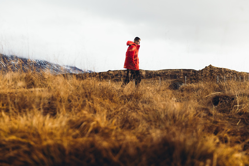 Young man in red jacket and eyeglasses meets the scenic sunrise walking at the orange bright landscape with Mountain View in Iceland