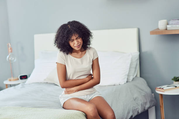 Oh body, why have you betrayed me? Shot of a young woman suffering from stomach cramps in her bedroom irritable bowel syndrome stock pictures, royalty-free photos & images