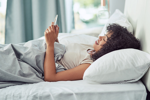 Shot of a beautiful young woman using a smartphone while relaxing in her bed in the morning