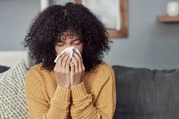 Shot of a young woman blowing her nose with a tissue at home