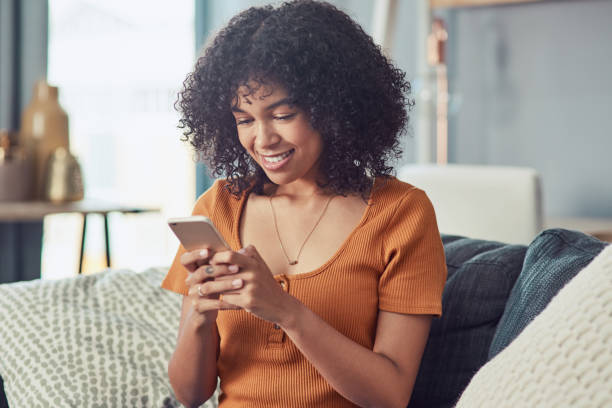 Keeping her social media fans updated Shot of a young woman using a smartphone on the sofa at home Stream stock pictures, royalty-free photos & images