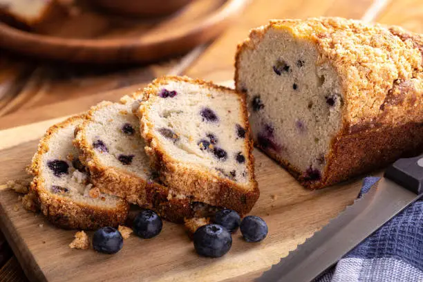 Closeup of a loaf of sliced blueberry streusel sweet bread with fresh berries on a wooden cutting board