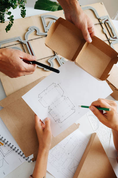istock Box makers working behind a table, discussing schematics of a box 1217589003