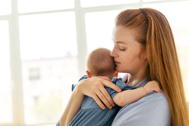 junge mutter mit einem drei monate alten baby am fenster im schlafzimmer, nachdenklich und müde - new mother stock-fotos und bilder