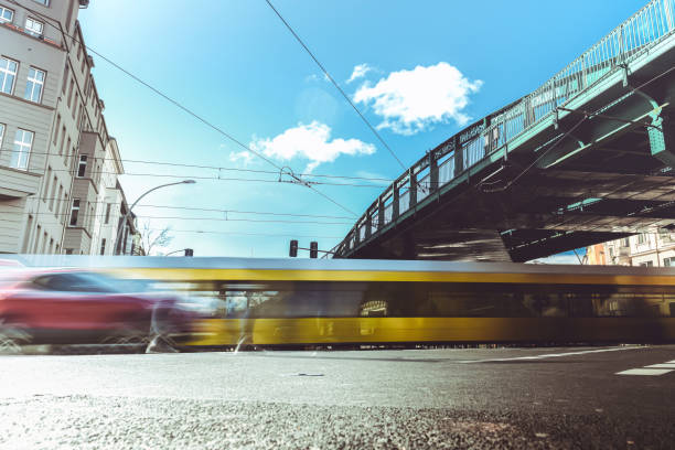 long exposure of yellow tram and cars passing intersection under elevated railway in Berlin Prenzlauer Berg