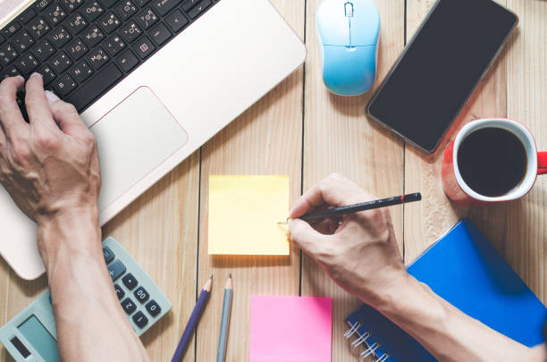 istock top view working desk. business man work on workspace use pencil writing a sticky note with copy space on wood table. 1217597341