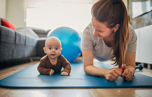 Two people, young mother exercising together with her baby son at home.