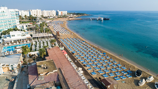 Aerial bird's eye view of Sunrise beach at Fig tree in Protaras, Paralimni, Famagusta, Cyprus. The famous tourist attraction family bay with golden sand, boats, sunbeds, restaurants, water sports, people swimming in sea on summer holidays, from above.