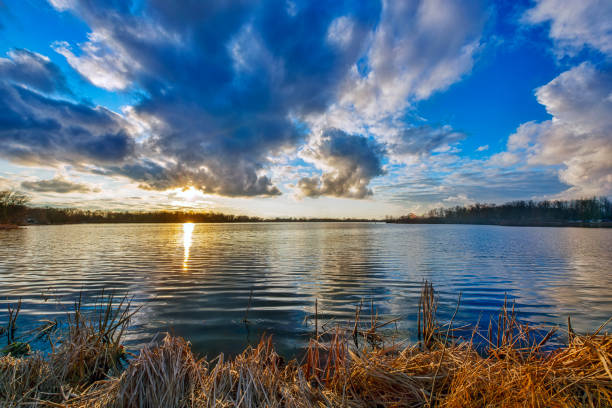 Sunset over quiet lake with Clouds and sun on the horizon.