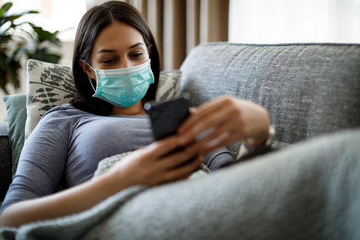 Sick woman with face protective mask using mobile phone