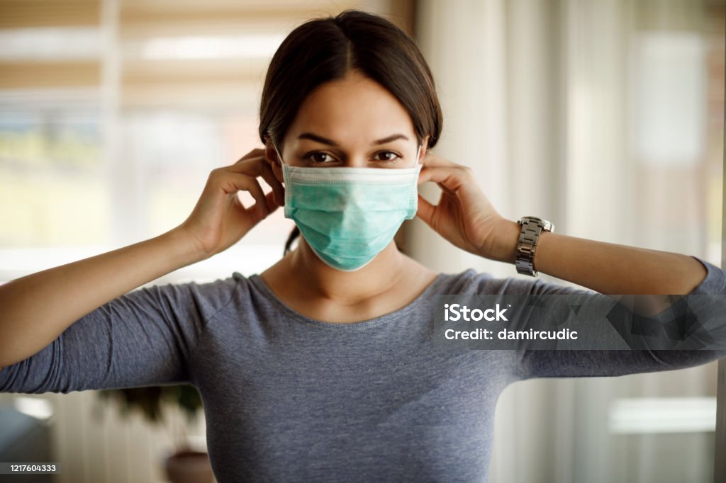 Portret van jonge vrouw die op een beschermend masker voor coronavirusisolatie zet - Royalty-free Beschermend masker - Werkkleding Stockfoto