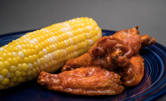 Photography of spicy hot wings and corn on the cob.