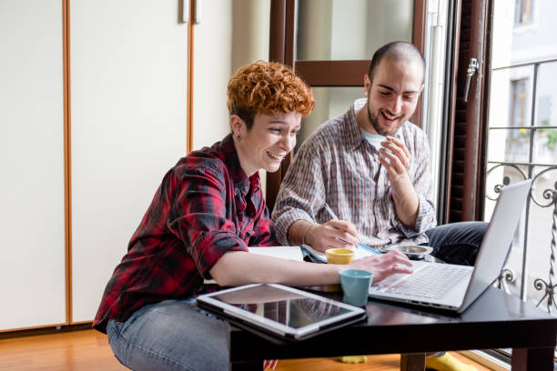 Two young man and woman working indoor in house using computer stock photo