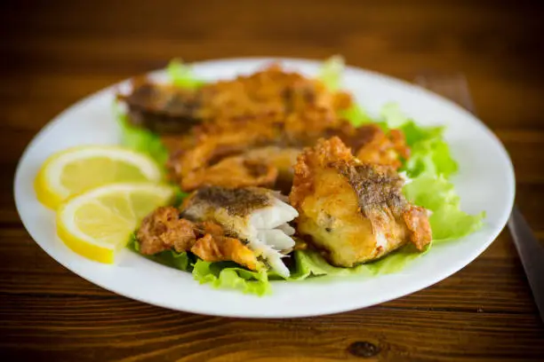 fried hake fish in batter with lettuce and lemon in a plate on a wooden table