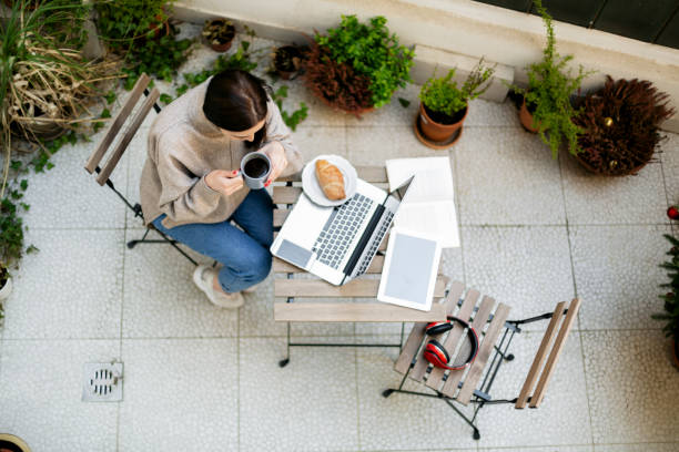 Young woman working from home Aerial view of a young woman prepping her work space at her apartment terrace, setting up a light lunch and getting ready to work from home on her laptop, top view building terrace photos stock pictures, royalty-free photos & images