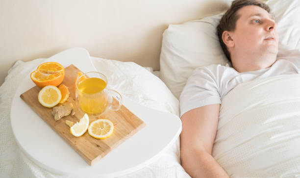 Cup with antipyretic drugs for colds,flu.Sick man in bed. Tea with citrus vitamin C,ginger root,lemon,orange.Wooden tray. Home self-treatment.Medical quarantine antiviral covid-19 coronavirus therapy. taza con medicamentos antipiréticos para resfriados, gripe. enfermo en la cama. té con vitamina c cítrica, raíz de jengibre, limón, naranja. bandeja de madera. autotratamiento en el hogar. terapia médica de cuarentena antiviral cóvido-19 coronavirus