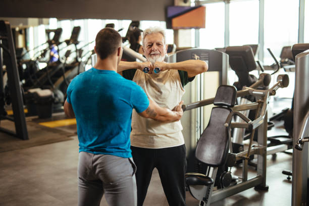 istock Senior man exercising with personal trainer using dumbbells at the gym 1217609560