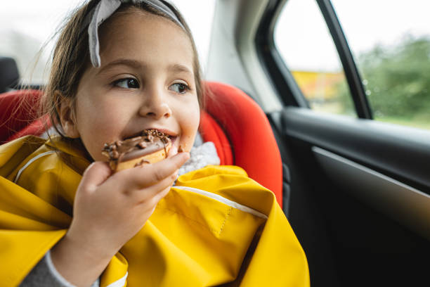 istock Beautiful young child biting a doughnut on a back seat of a car 1217611119