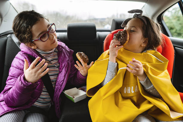 Cute carefree children enjoying doughnuts on the back seat of a car Carefree siblings, sisters, enjoying their time together on the back seat of a car during a road trip. back seat photos stock pictures, royalty-free photos & images