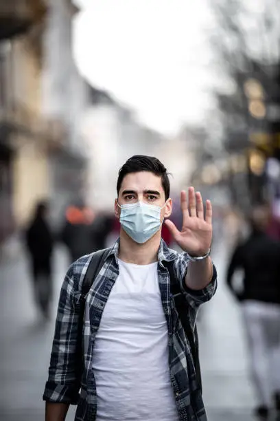 Photo of Portrait of young Man, saying no to coronavirus infection with wearing medical surgical blue face mask