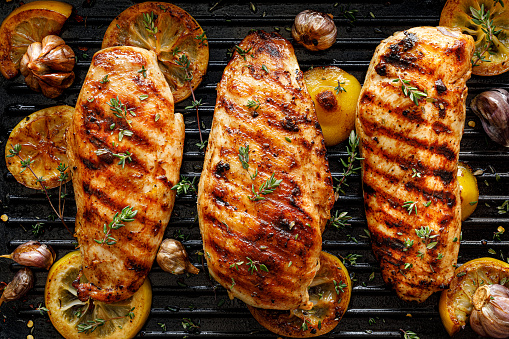 Grilled chicken breasts with thyme, garlic and lemon slices on a grill pan close up, top view