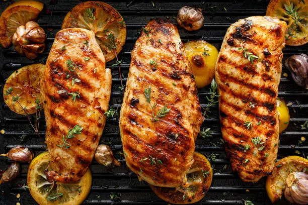 Grilled chicken breasts with thyme, garlic and lemon slices on a grill pan close up, top view