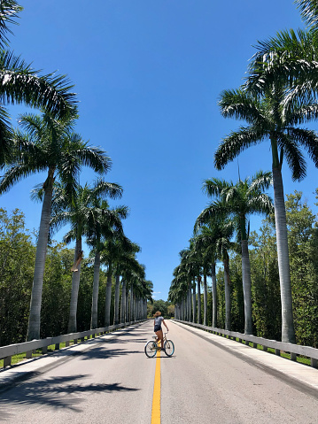 Girl riding her bike down beautiful tropical road in souther USA.