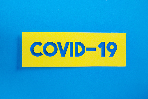 Yellow Sticky Paper With Covid-19 Message On Blue Background. Horizontal composition with copy space.