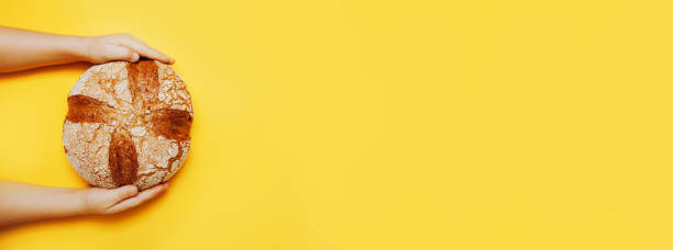 istock Tasty big round bread in child's hands on yellow background. 1217618078