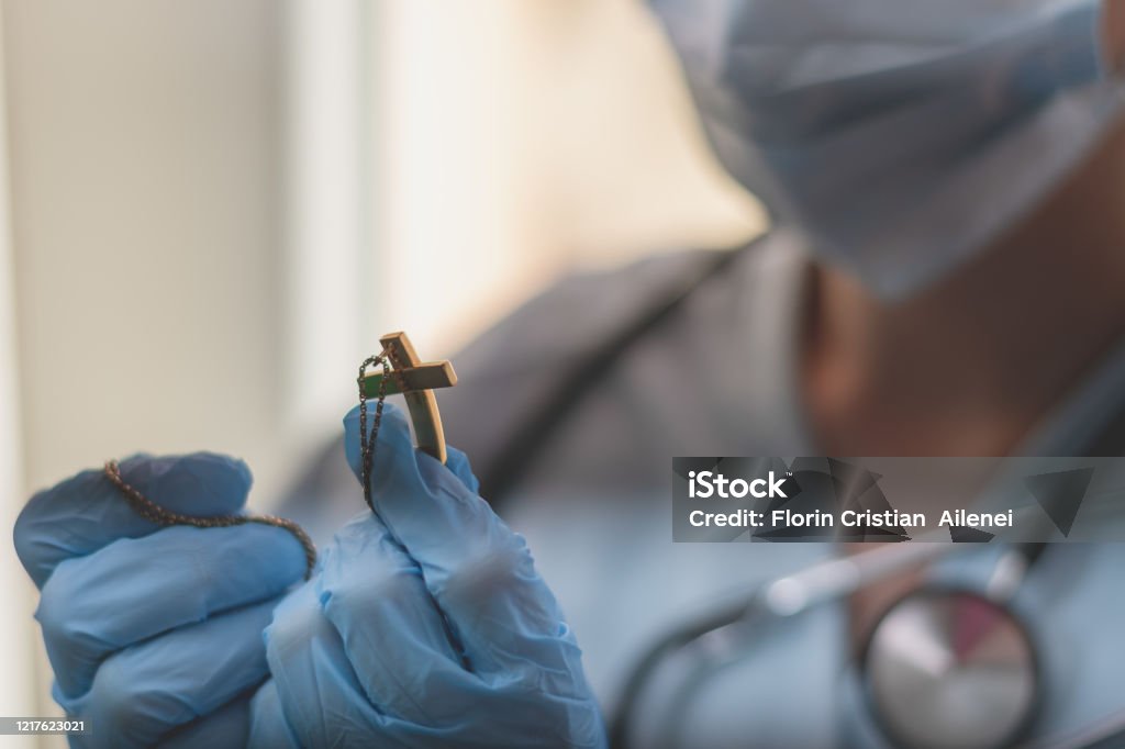 female doctor praying young medical worker is holding a crucifix in her hand and she is praying Catholicism Stock Photo