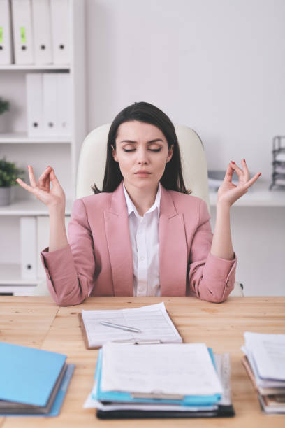 istock Young serious female office manager practicing yoga by desk at break 1217629296