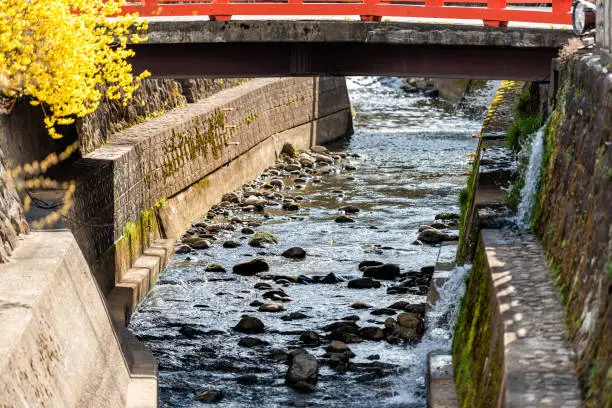 Small red vermilion colorful bridge by Enako river with rocks in Takayama, Gifu prefecture in Japan with water in spring and yellow tree