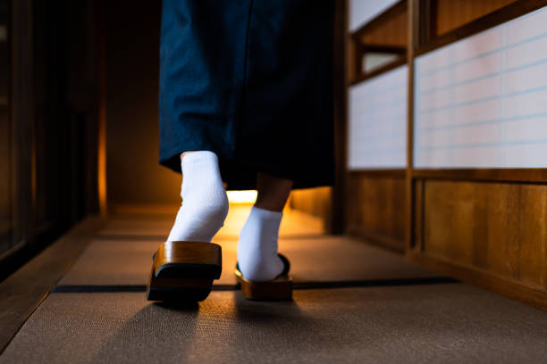 Japanese ryokan traditional house with man in kimono back closeup of legs feet with tabi white socks and geta shoes walking by shoji sliding paper doors and tatami mat floor Japanese ryokan traditional house with man in kimono back closeup of legs feet with tabi white socks and geta shoes walking by shoji sliding paper doors and tatami mat floor geta sandal stock pictures, royalty-free photos & images