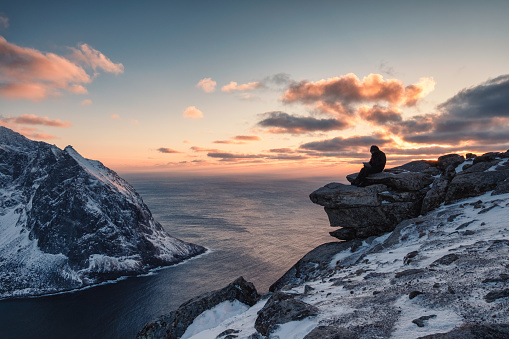 Traveler working a laptop on Ryten mountain on sunset at Lofoten Islands, Norway