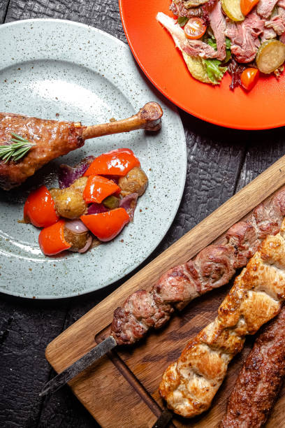 istock background black burnt carbonized forest, structure, wooden cutting board, turkey drumstick on a plate, skewers of different meat, grilled vegetables and fresh on a red plate 1217635367