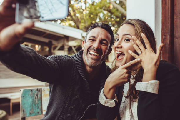 Beautiful engaged couple making selfie Affectionate couple announcing their engagement with selfies while sitting at cafe. Happy couple taking a selfie and showing off their wedding ring at coffee shop. engagement ring stock pictures, royalty-free photos & images