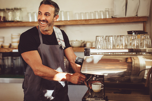 Smiling barista making espresso with a coffee maker