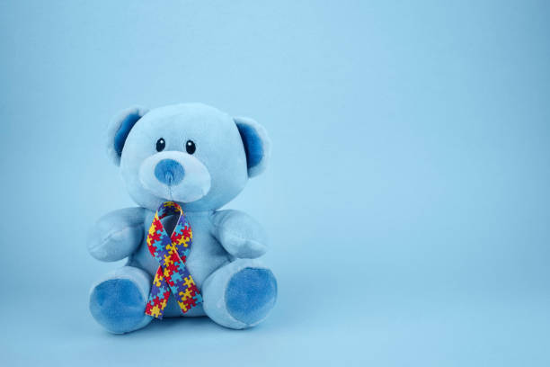 World Autism Awareness, concept with teddy bear holding puzzle or jigsaw pattern ribbon on blue background