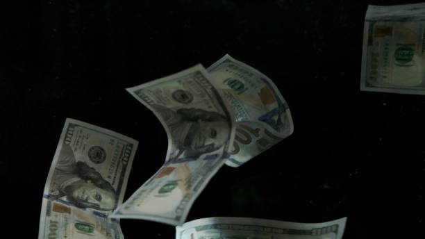 istock Falling flying american dollar banknotes on a black background 1217642365